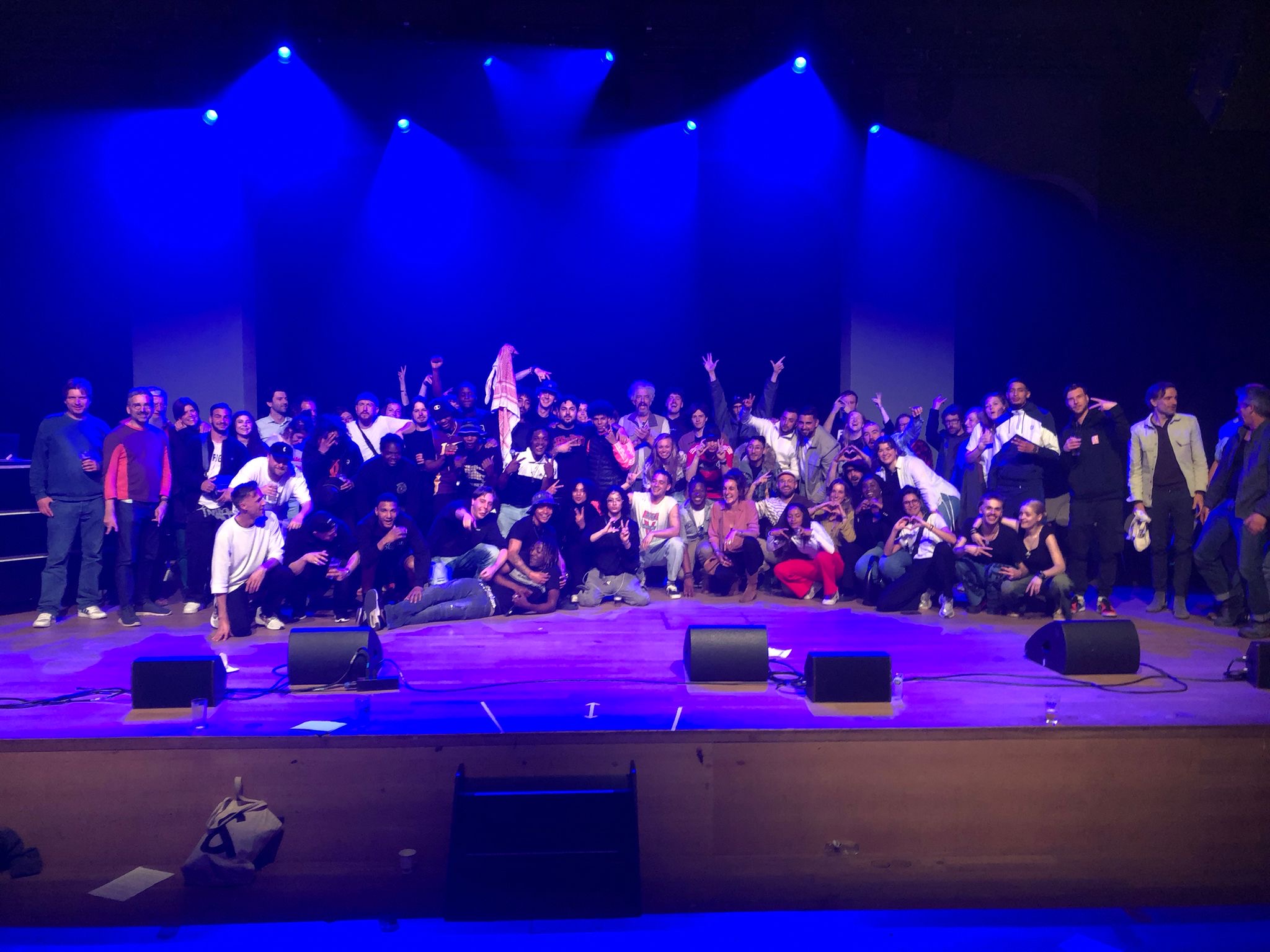 Gent x Vila Cruzeiro slotmoment grote groep betrokken jongeren en projectmedewerkers op podium onder blauw licht