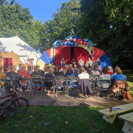 zicht op zittend publiek en buitenpodium, en een circustent