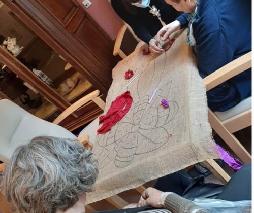 2 oude en 1 jonge vrouw werken aan een borduurwerk met bloemafbeelding
