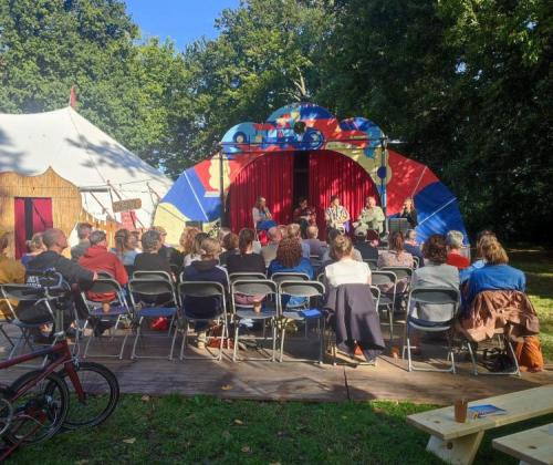 Uitwijken_inspiratiedag 2025 zicht op zittend publiek en buitenpodium, en een circustent