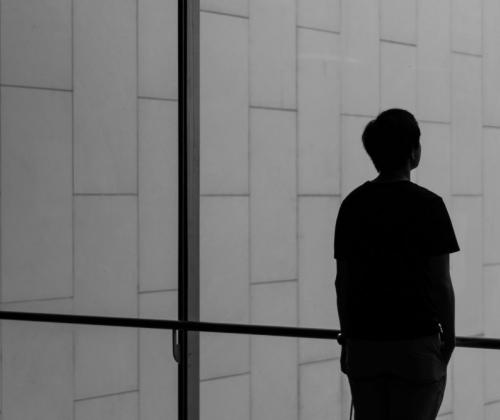 silhouet van jongeman die door groot raam kijkt